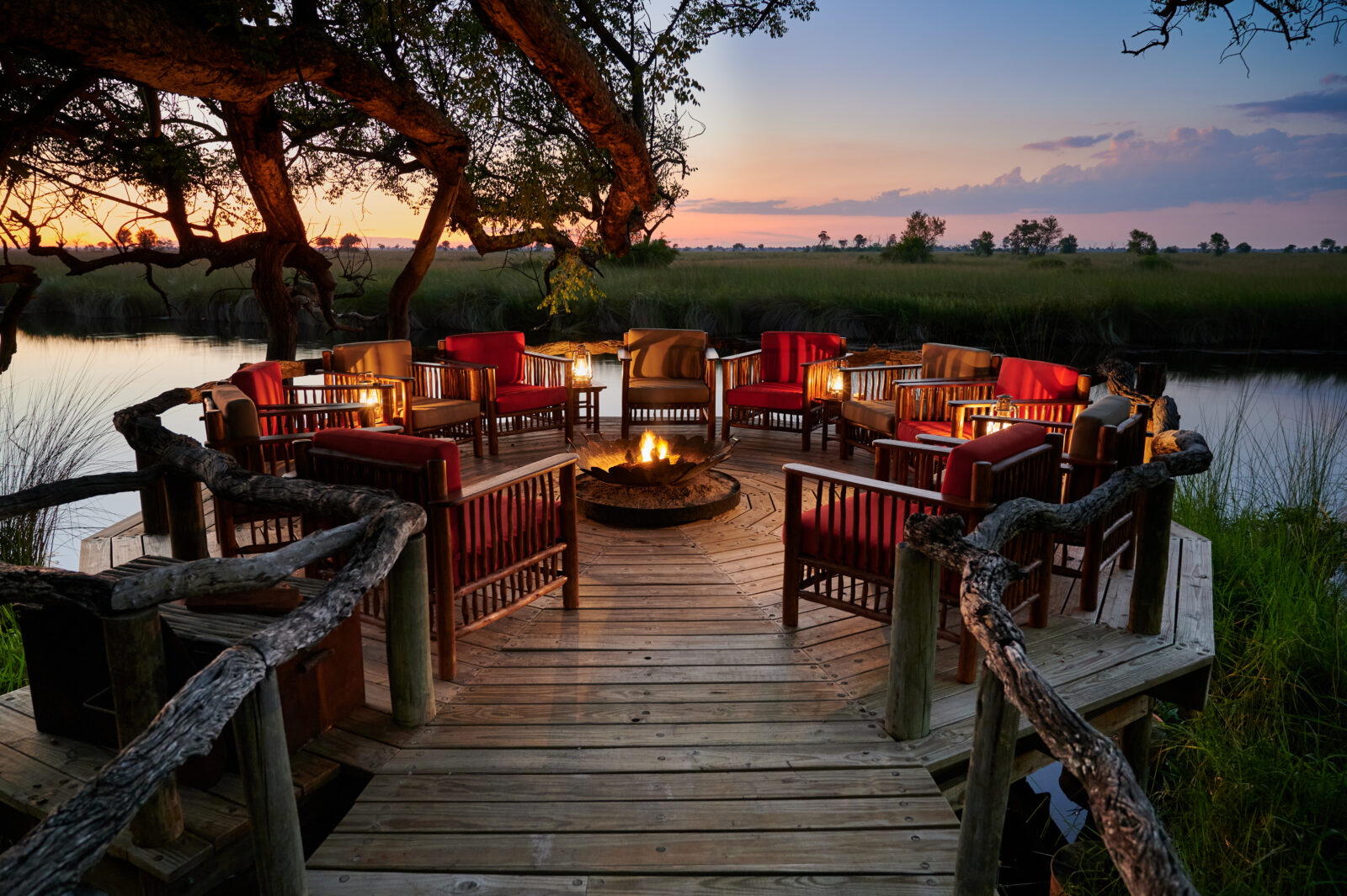 Armchairs around a lit fire on the timber deck overlooking the channel at Camp Xakanaxa, Moremi Game Reserve, Botswana
