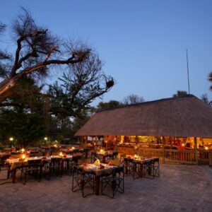 The lit thatched restaurant, bar and deck under mokolwane palms at Nata Lodge, Botswana, at dusk