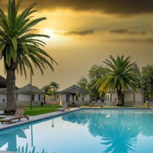 The swimming pool, palms and thatched rooms at Kalahari Arms Hotel in Ghanzi, Botswana