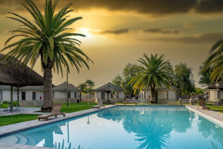 The swimming pool, palms and thatched rooms at Kalahari Arms Hotel in Ghanzi, Botswana