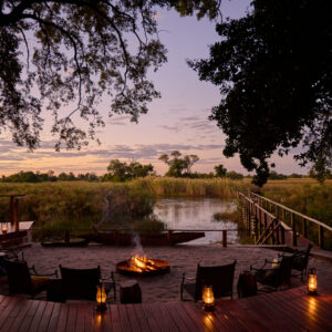 A lantern-lit fire circle on the deck above the Nxamaseri Channel at dusk, Okavango Panhandle, Botswana