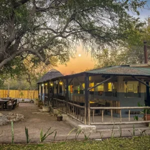 The lit main building and outdoor fire circle under camelthorn trees at Thakadu Bush Camp near Ghanzi, Botswana