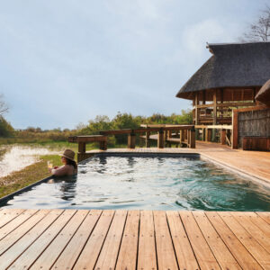 The timber pool deck and thatched main area looking out over a Delta channel at Camp Okavango, Okavango Delta, Botswana