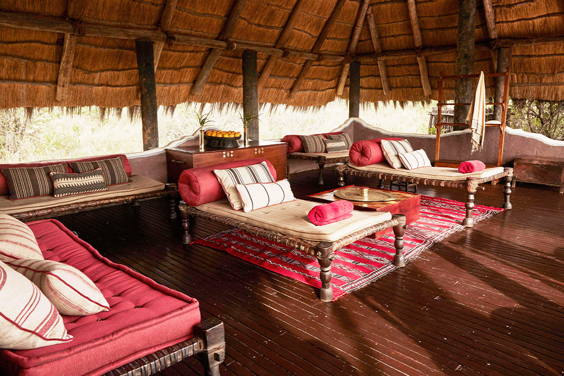Low cushioned seating and rugs in the shaded thatched lounge at Camp Kalahari, Makgadikgadi, Botswana