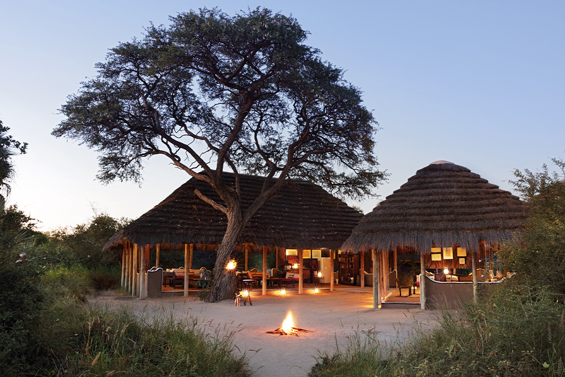 The thatched main area and fire of Camp Kalahari under acacias on Brown Hyena Island, Makgadikgadi, Botswana