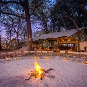 A fire burning in front of the lantern-lit open main area at Kwara Camp, Kwara Concession, Okavango Delta, Botswana