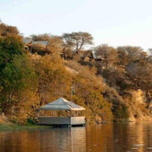 The clifftop tents of Meno a Kwena above the Boteti River with the floating photographic hide moored below, Makgadikgadi, Botswana