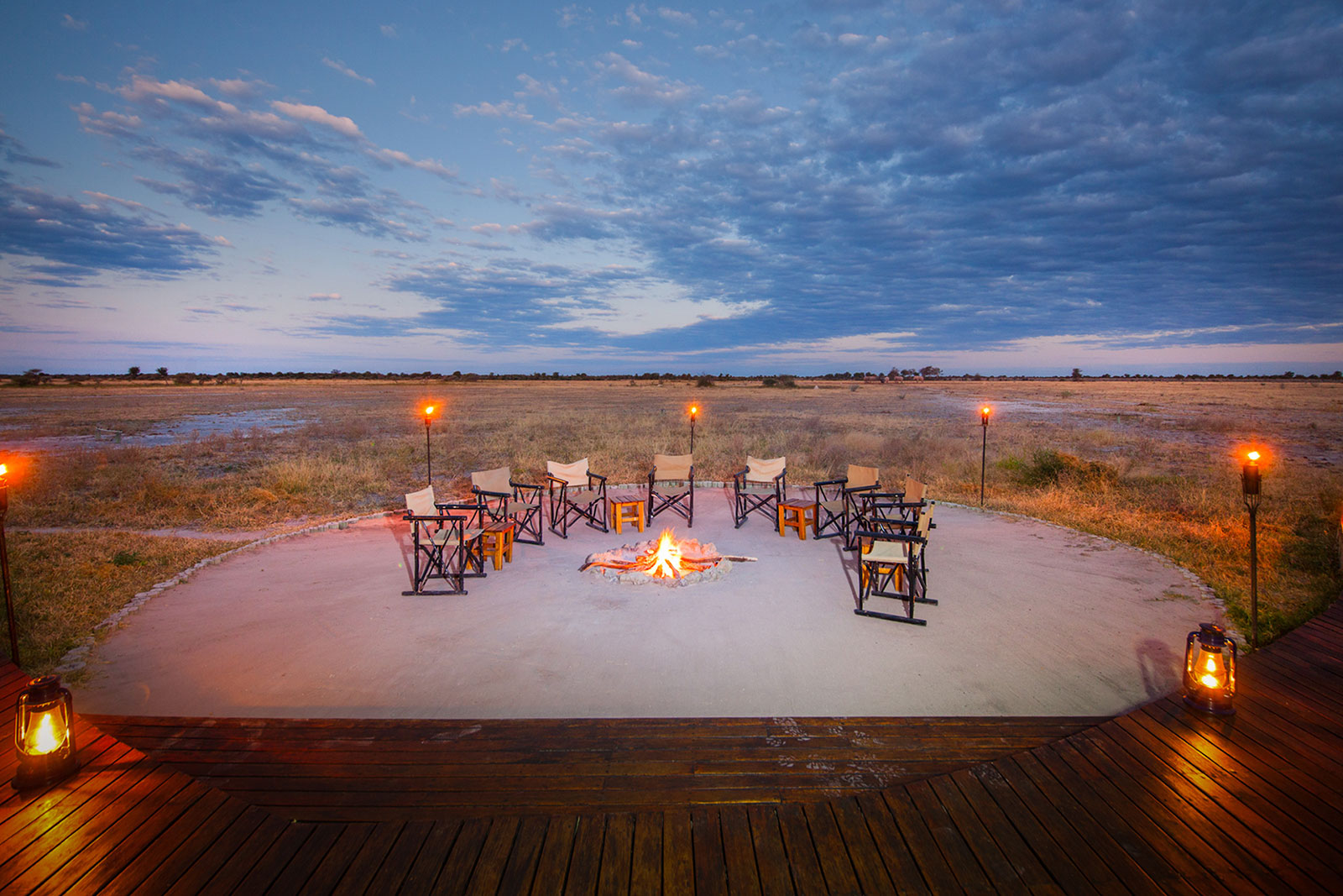 A lantern-lit fire circle on the deck at Nxai Pan Camp looking across the pan grassland, Botswana