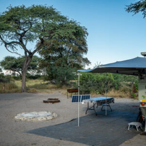 A vehicle with an awning, fire ring and table on a cleared campsite pitch under an acacia at Kumaga campsites on the Boteti River, Botswana