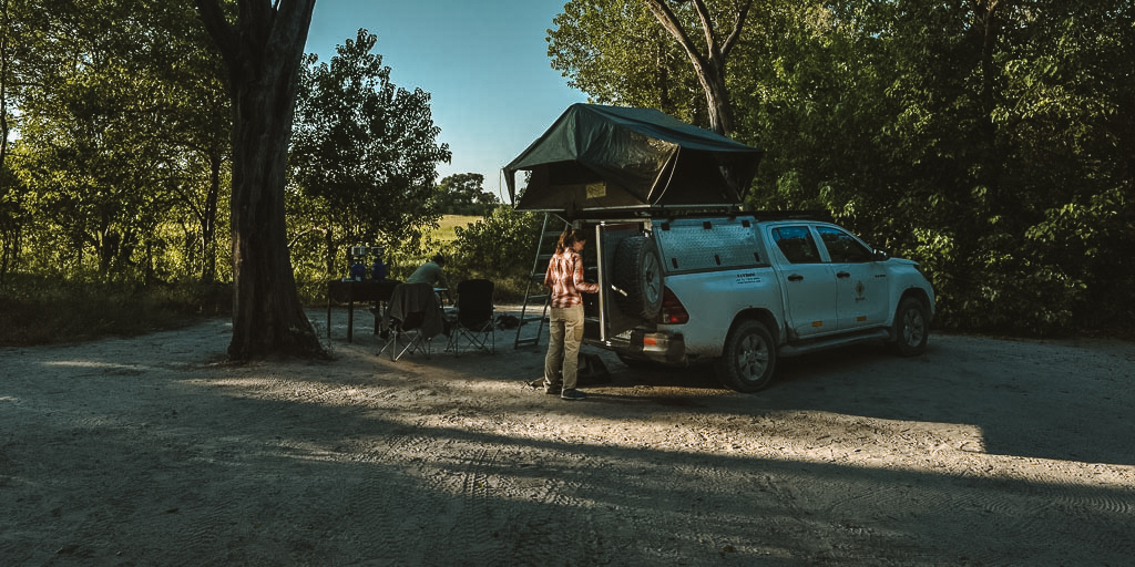 A vehicle with a rooftop tent pitched under mature riverine trees at the SKL Khwai campsites near Moremi North Gate, Botswana