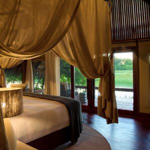 A tent bedroom with a draped four-poster bed and doors onto the Khwai River deck at Sediba Sa Rona, Khwai, Botswana