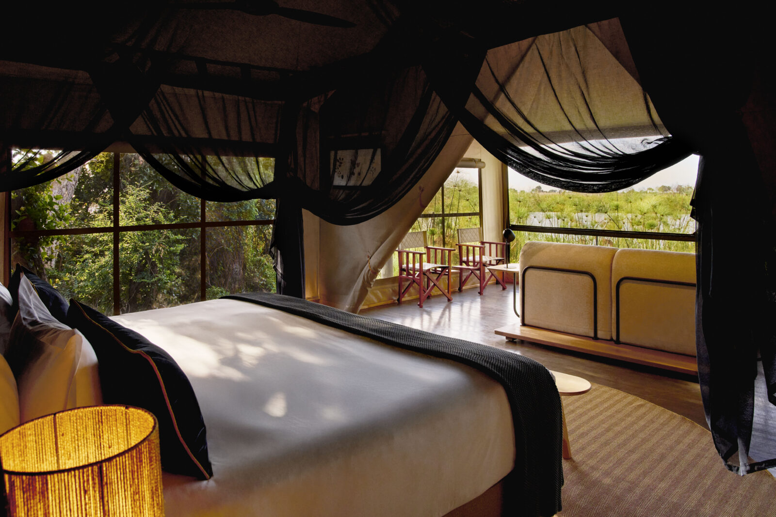 A mosquito-netted bed and lagoon-facing windows in a tent at Xugana Island Lodge, Okavango Delta, Botswana