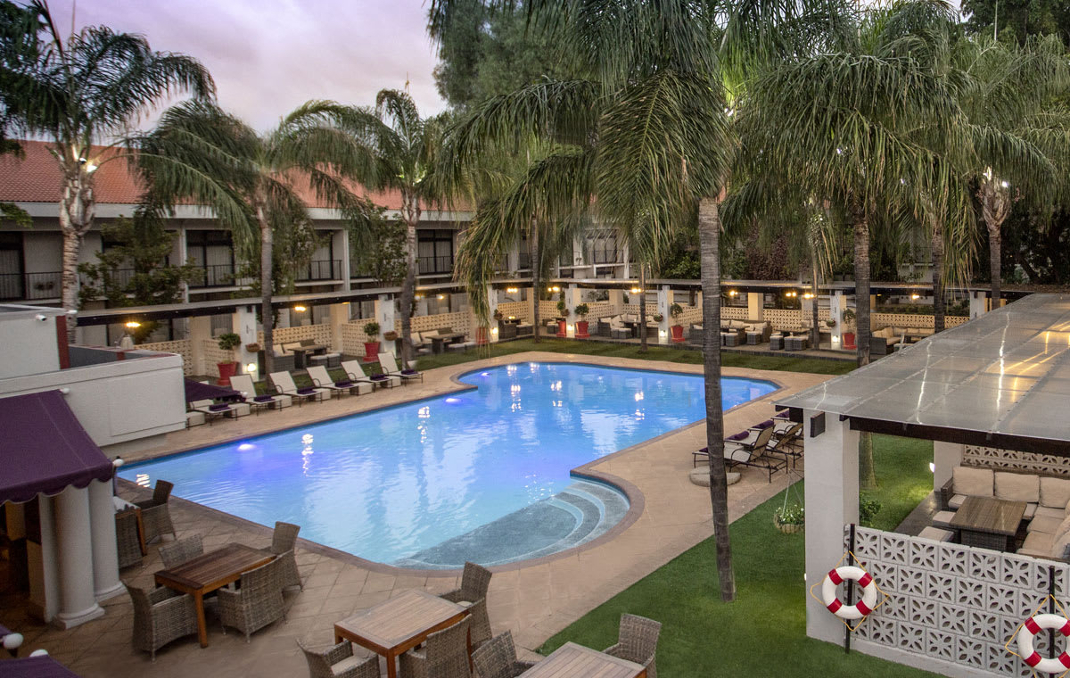 The lit swimming pool, loungers and palms in the courtyard of Avani Gaborone Resort and Casino, Gaborone, Botswana