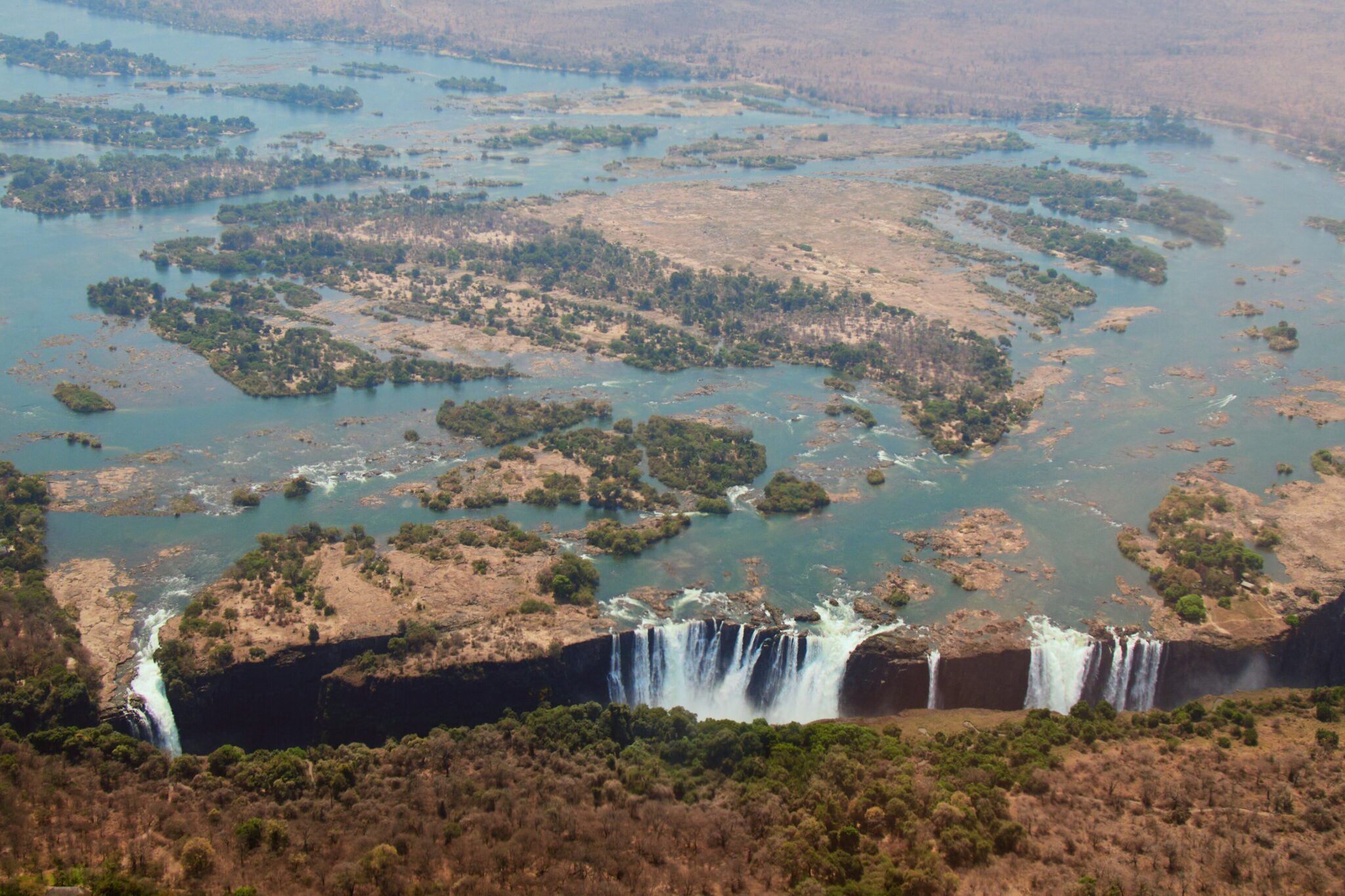 Aerial view of Victoria Falls on the Zambezi River, with water falling along the lip and braided channels and islands upstream