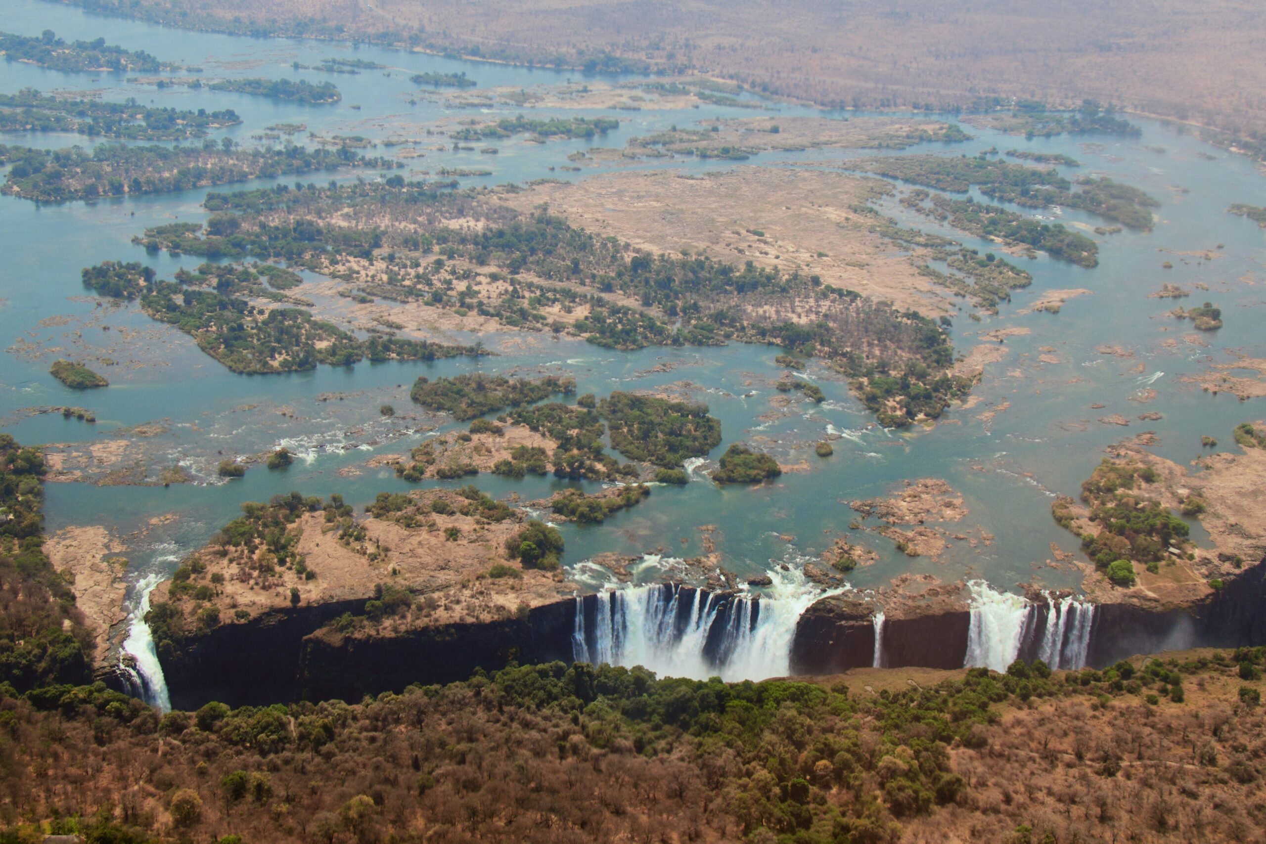 Aerial view of Victoria Falls on the Zambezi River, with water falling along the lip and braided channels and islands upstream