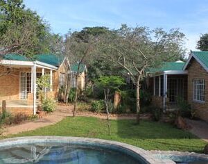 Green-roofed self-catering cottages around a lawn and swimming pool at Chobe River Cottages in Kasane, Botswana