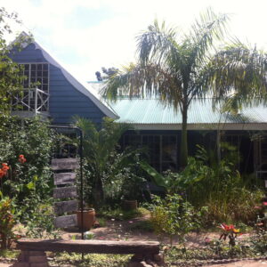 The green-roofed guesthouse buildings of The Old House surrounded by palms and tropical planting in Kasane, Botswana
