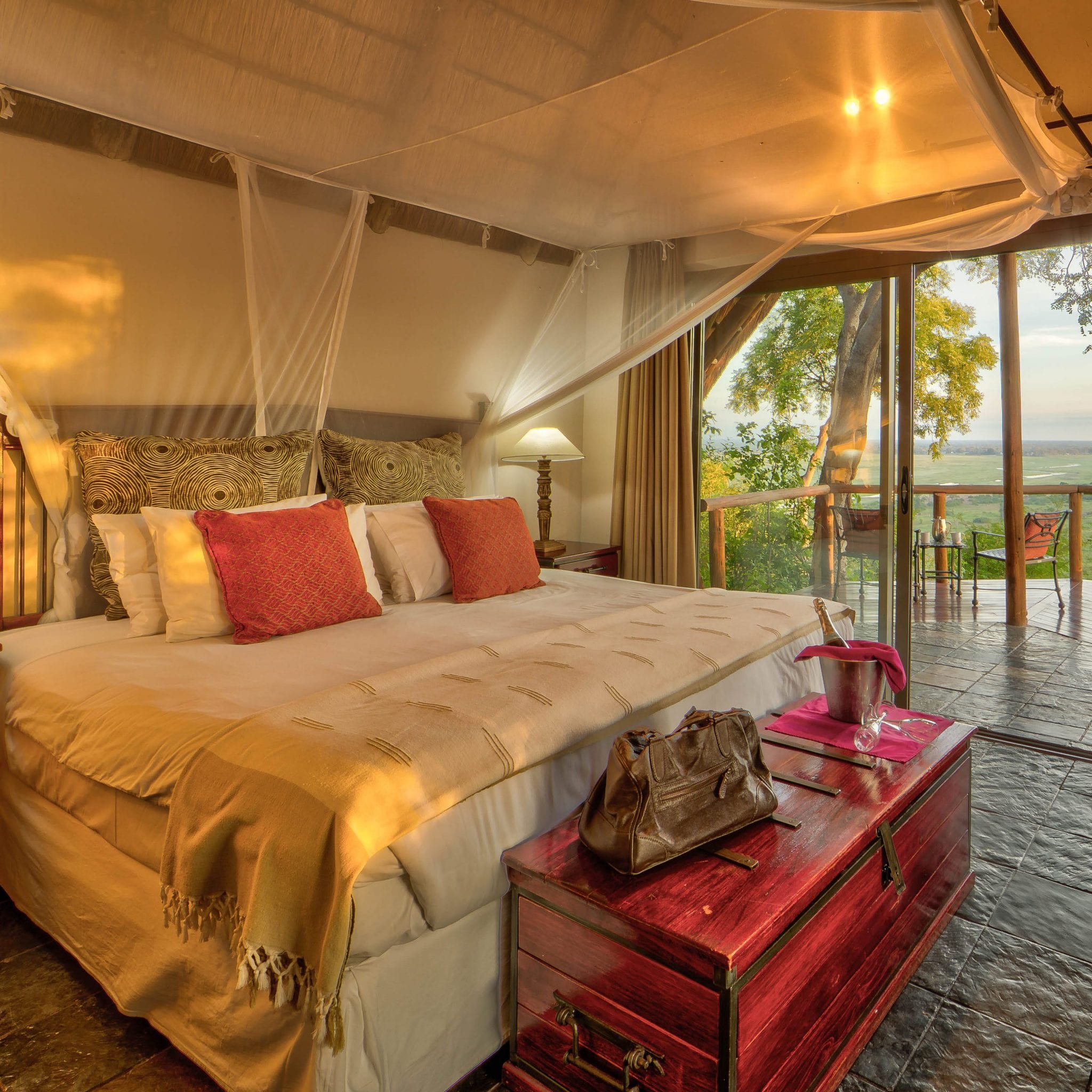 A cottage bedroom with a mosquito-netted bed opening onto a deck above the Chobe floodplain at Muchenje Safari Lodge, Botswana